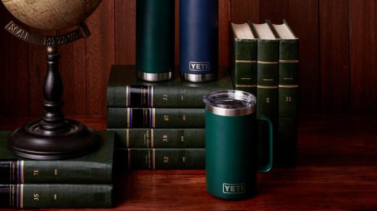 neatly stacked and organized dark green books against a dark dark wood background on a wood table with 3 YETI tumblers featured